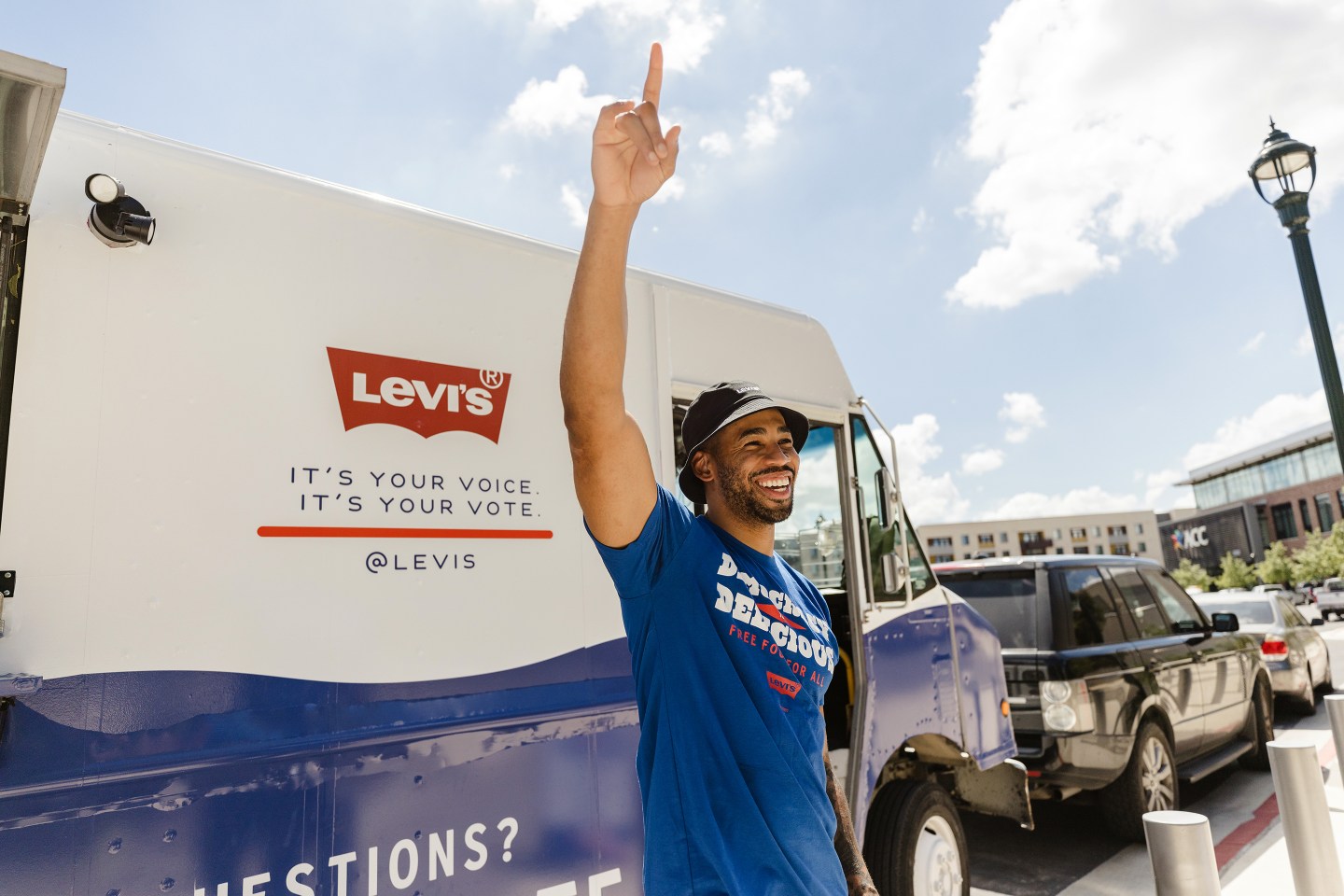 Man celebrating with arm up in front of a truck with Levi&#039;s logo as part of their voter registration initiative.